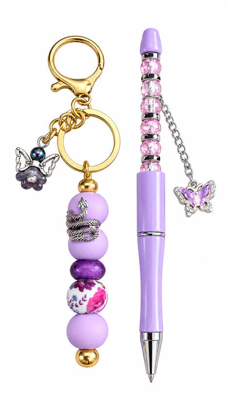 A mystical purple stationery set showing a matching gold-hardware keychain and lavender ballpoint pen, featuring a detailed silver snake wrap, a pink floral bead, a dangling purple flower-angel charm, and a rhinestone butterfly chain charm.