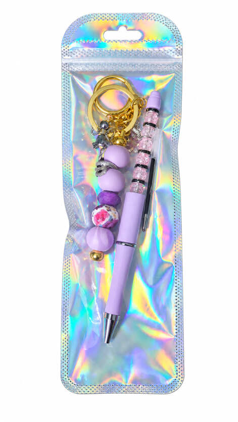 A lavender dusk and mystic snake beaded pen and matching gold keychain set displayed inside a glossy, iridescent holographic retail pouch.