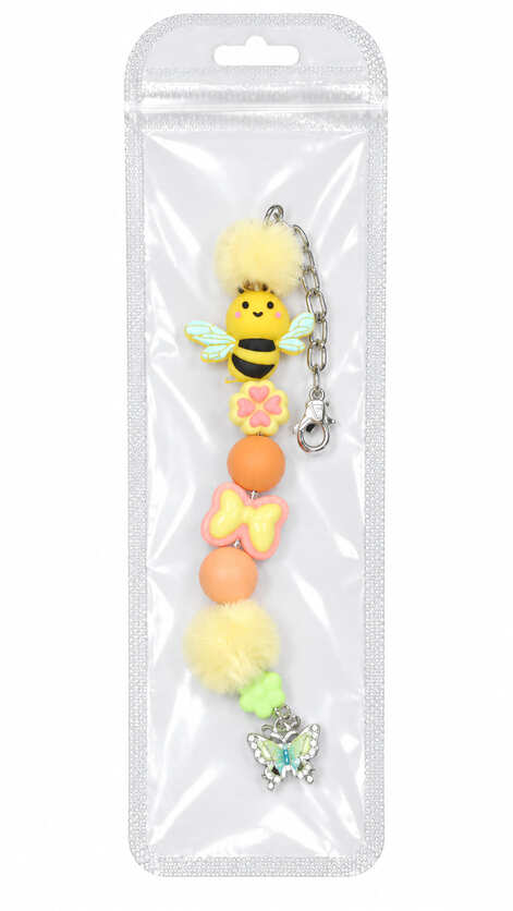 A bright yellow honey bee and pink flower silicone beaded fidget charm with fuzzy pom-poms, displayed inside a clear, professional retail plastic pouch with a hanging tab.