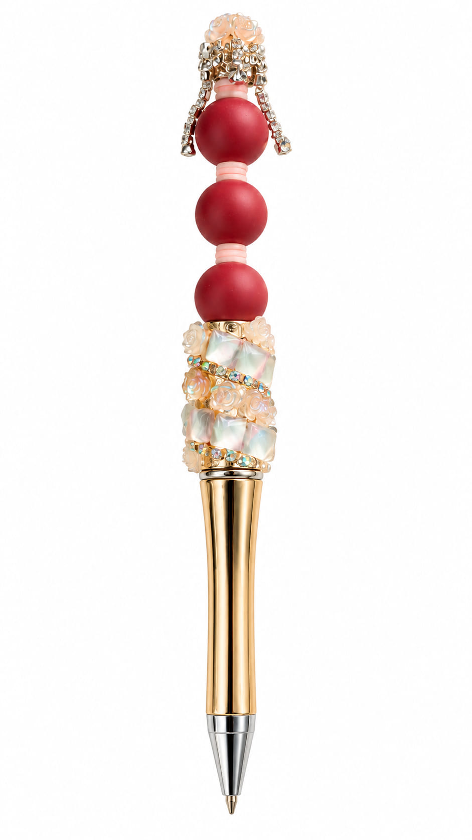 A close-up view of a luxury custom ballpoint pen with a curved metallic gold barrel, decorated with iridescent opalescent square beads, miniature peach resin roses, rows of crystals, three matte crimson red silicone spheres, and a rhinestone crown topper.