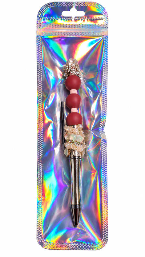 A luxury gold custom beaded pen decorated with crimson beads, resin roses, and crystals, packed inside a shimmering, iridescent holographic retail pouch alongside a spare black ink refill.