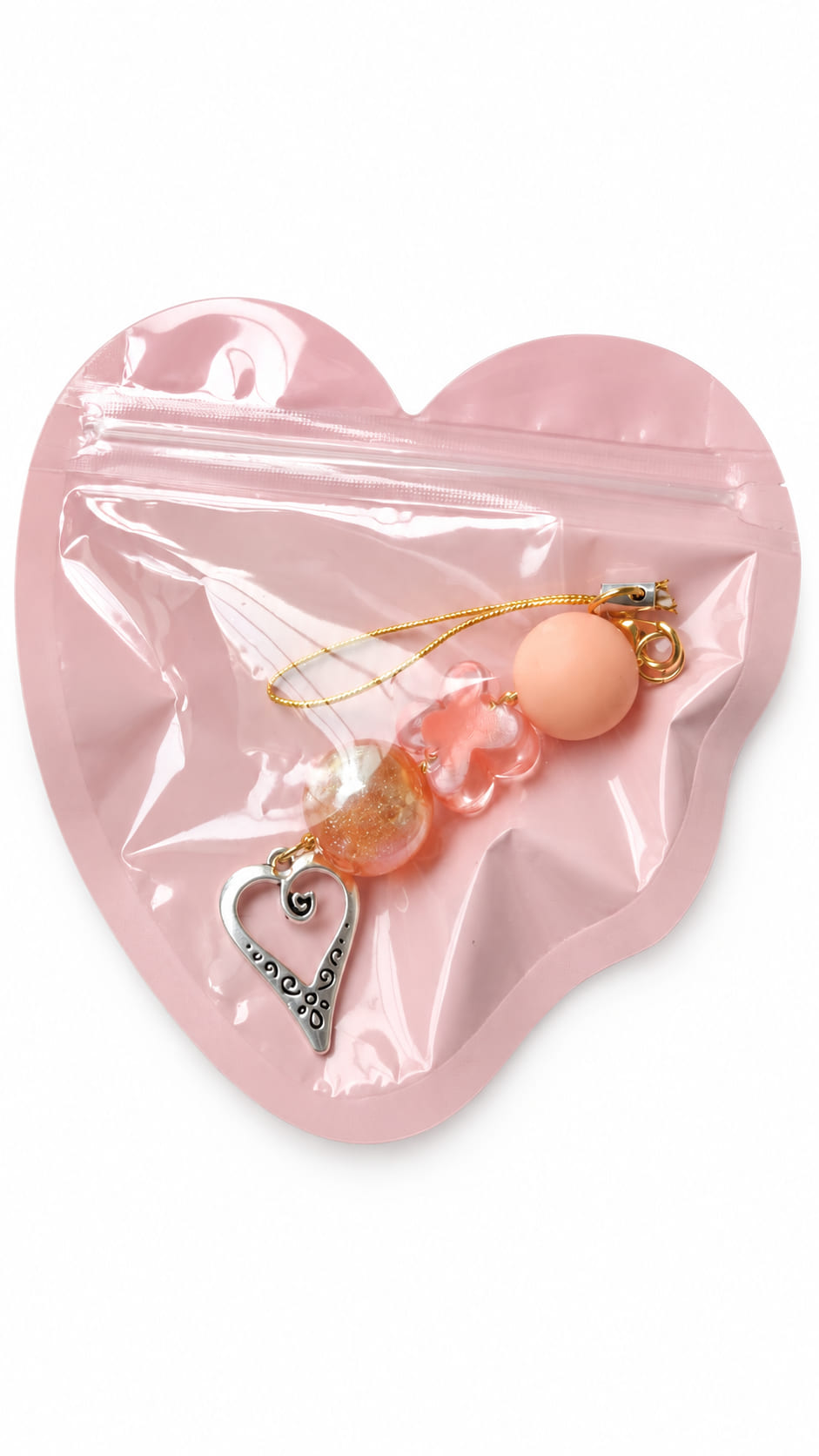 A close-up studio photograph of a handmade beaded phone strap keychain presented inside a protective, translucent pastel pink heart-shaped zip-lock packaging pouch against a crisp white backdrop.