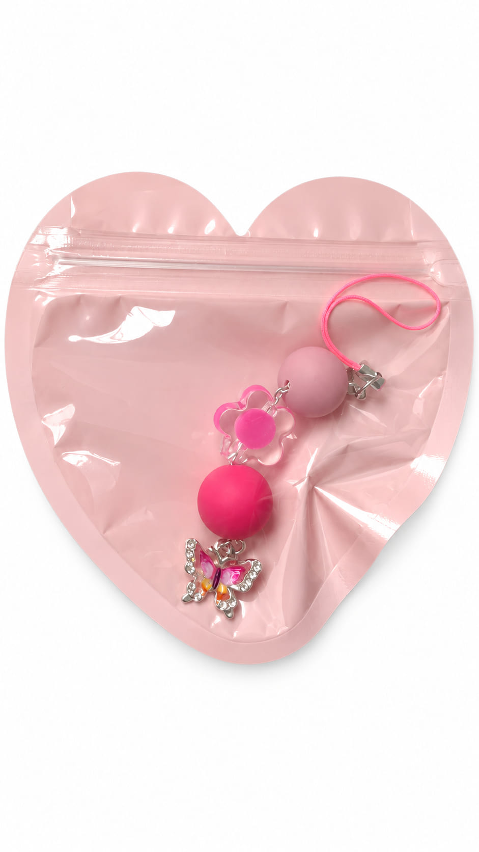 A close-up studio photograph of a handmade beaded phone strap keychain presented inside a protective, translucent pastel pink heart-shaped zip-lock packaging pouch against a crisp white backdrop.