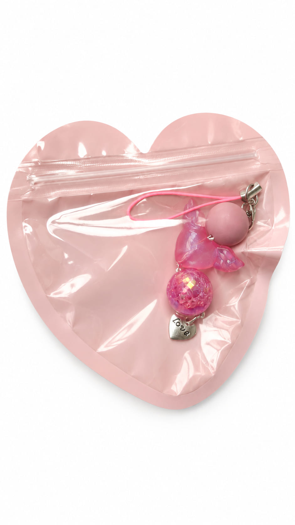 A close-up studio photograph of a handmade beaded phone strap keychain presented inside a protective, translucent pastel pink heart-shaped zip-lock packaging pouch against a crisp white backdrop.