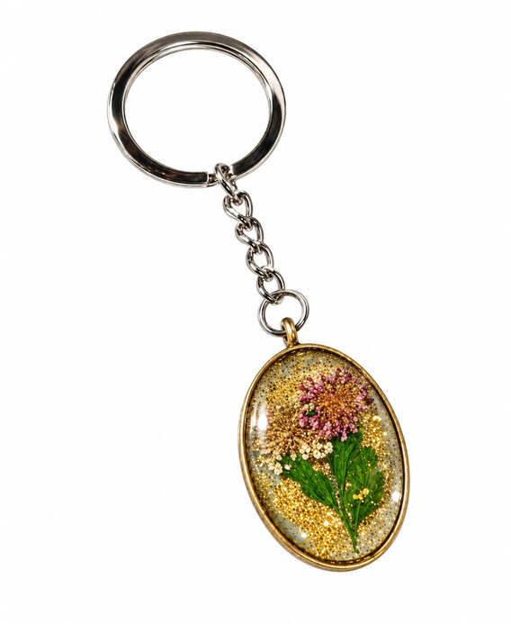 An artisan oval vintage flower resin keychain featuring real pressed pink and white botanical blooms cast with shimmering gold glitter in a bronze bezel casing, attached to a classic silver metal keyring chain.