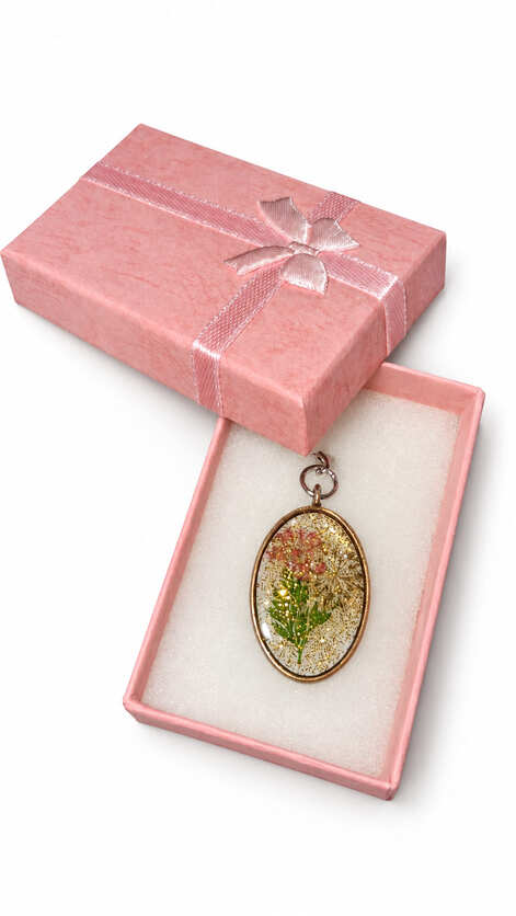 Handmade oval vintage bronze resin pendant with real pressed pink flowers and gold glitter flakes, displayed inside an elegant textured pink gift box with a matching satin ribbon bow.