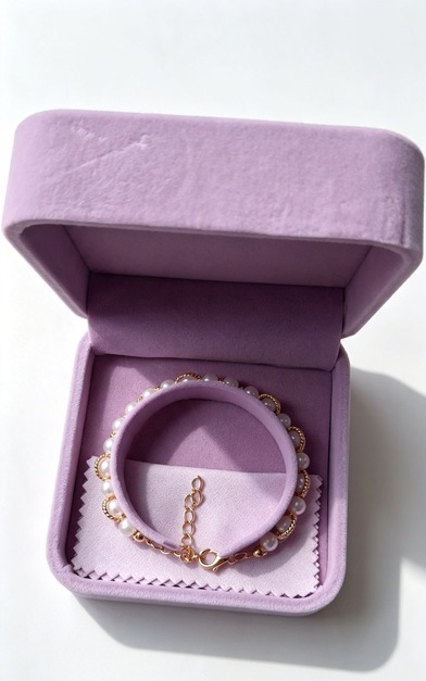 Luxury elegant wedding bracelet with white pearls and gold accents presented inside an open pastel purple velvet gift box with a matching polishing cloth.
