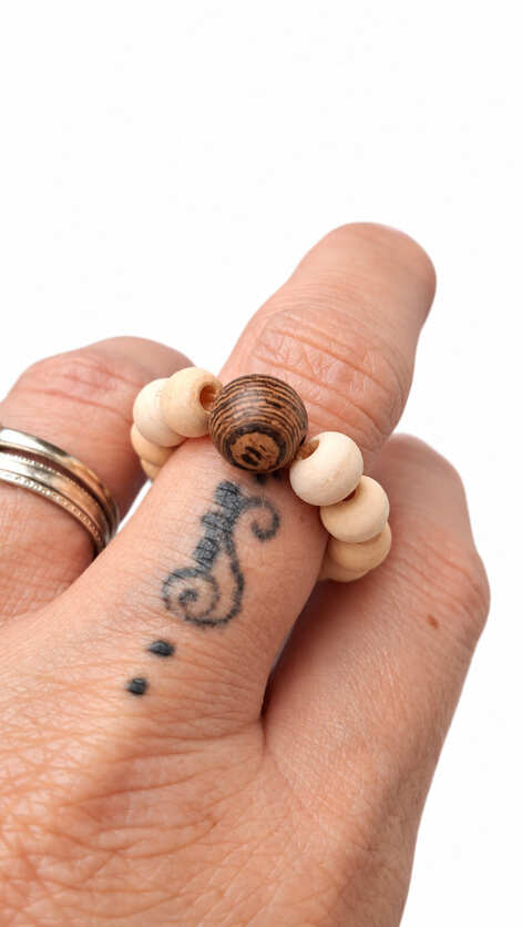 Handmade wooden bead ring worn on a finger showing the pale natural wood beads and contrasting dark wood focal bead.
