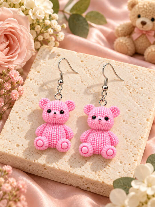 Pink teddy bear drop earrings with 925 sterling silver hooks styled on a cream stone surface with pink flowers and satin.