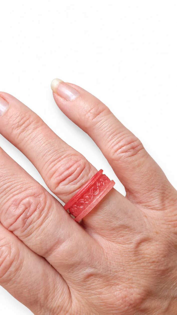 Close-up of handmade coral pink epoxy resin ring showing the detailed raised interwoven band design.