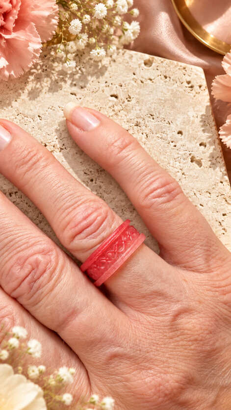 Coral pink handmade epoxy resin statement ring with decorative knot pattern shown worn on the hand.